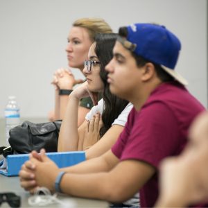 Three students listen to a presentation in class